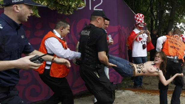 Polizisten tragen eine Frau mit nacktem Oberkörper bei einer Demonstration weg.