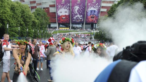 Eine Frau mit Blumenkranz sprüht Wasser vor dem Nationalstadion Warschau.