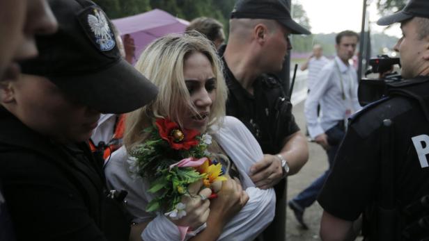 Eine Frau mit blonden Haaren und Blumen wird von Polizisten abgeführt.