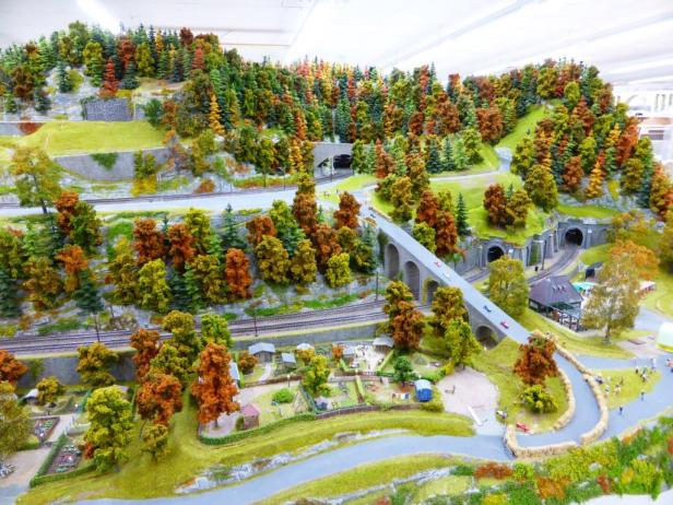 Eine Miniaturlandschaft mit Eisenbahnstrecke, Brücke und herbstlichen Bäumen.