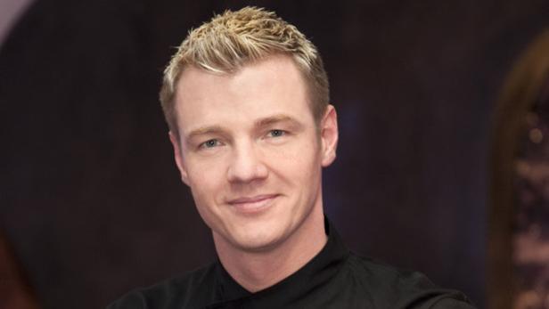 Ein Mann mit blonden Haaren lächelt in die Kamera.