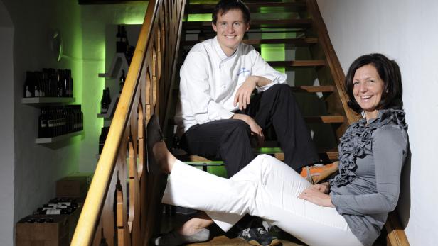 Ein Koch und eine Frau sitzen lächelnd auf einer Holztreppe.