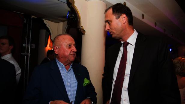 Zwei Männer in Anzügen unterhalten sich auf einer Veranstaltung.