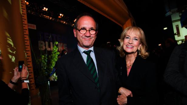 Ein Mann mit Brille und Anzug posiert mit einer Frau mit blonden Haaren für ein Foto.