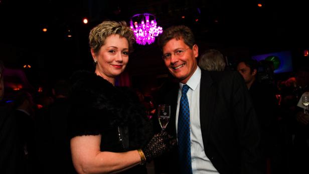 Eine Frau mit Stola und ein Mann im Anzug posieren mit einem Glas Sekt für ein Foto.