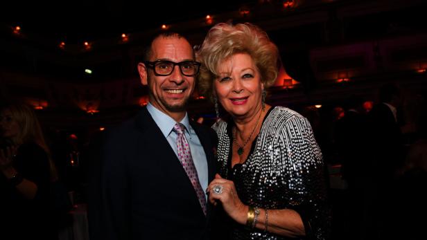 Ein Mann im Anzug und eine Frau in einem Paillettenoberteil posieren lächelnd für ein Foto.