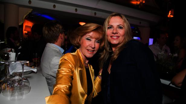 Zwei Frauen posieren lächelnd auf einer Party für ein Foto.