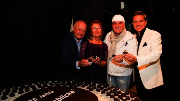 Eine Gruppe von Personen steht um eine große Torte mit kleinen Küchlein herum.