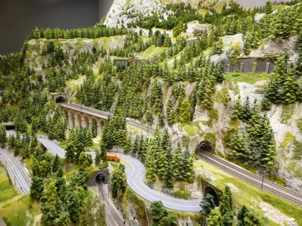 Eine Miniaturlandschaft mit Bergen, Tunnels, Eisenbahnschienen und einer kurvenreichen Straße.