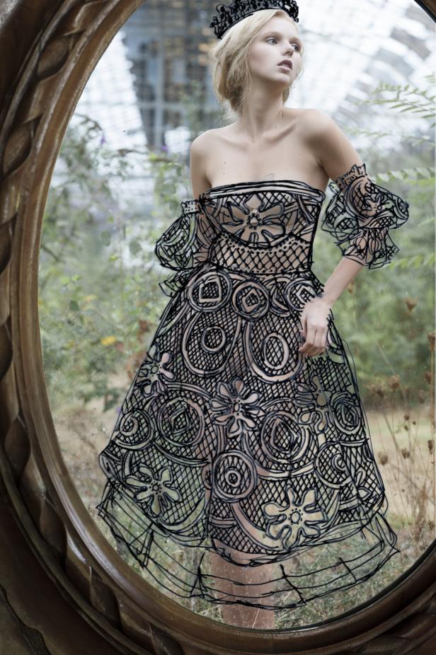 Eine Frau mit Krone und einem Kleid mit floralen Mustern, gesehen durch einen ovalen Rahmen.