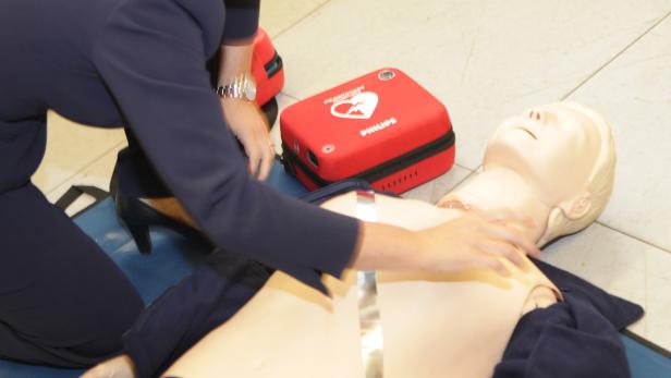 Eine Frau übt Wiederbelebung an einer Übungspuppe mit einem Defibrillator in der Nähe.