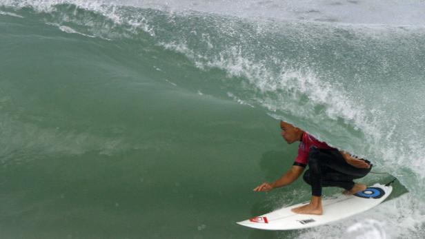Ein Surfer reitet auf einem Surfbrett unter einer brechenden Welle hindurch.