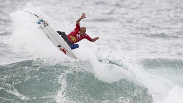 Ein Surfer springt mit seinem Board über eine Welle.