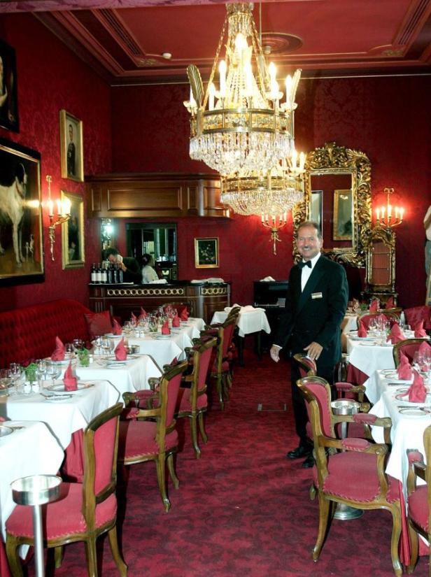 Ein Kellner steht in einem eleganten Restaurant mit roter Dekoration und Kronleuchtern.