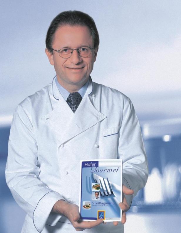 Ein Koch im weißen Kittel präsentiert ein „Hofer Gourmet“-Kochbuch.