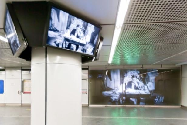 In einer U-Bahn-Station werden auf Bildschirmen und einer Wand historische Schwarzweißaufnahmen gezeigt.