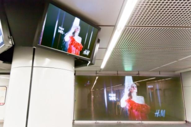 In einer U-Bahn-Station wirbt H&M auf Bildschirmen für ein rotes Kleid.