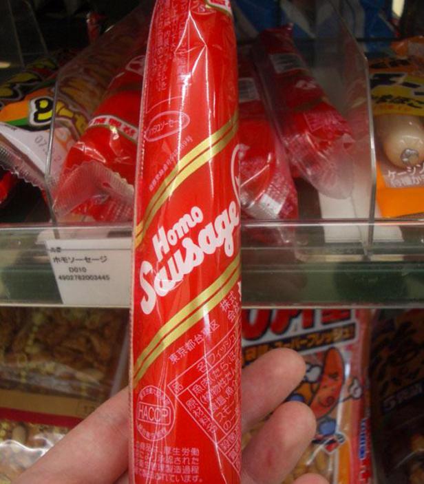 Eine „Homo Sausage“ in roter Verpackung mit goldenen Streifen wird in der Hand gehalten.