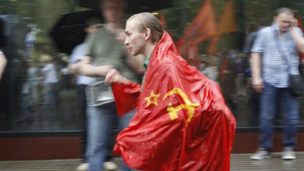 Ein Mann trägt eine rote Flagge mit Hammer und Sichel bei einer Demonstration.