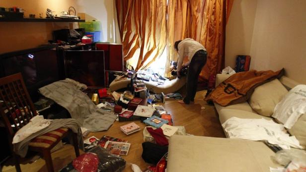 Eine Person beugt sich in einem unordentlichen Wohnzimmer über einen Hocker.