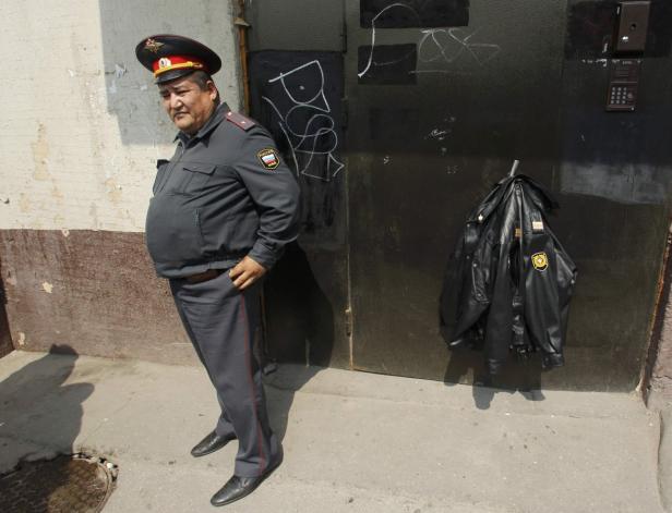 Ein russischer Polizist steht vor einer Tür, an der eine Jacke hängt.