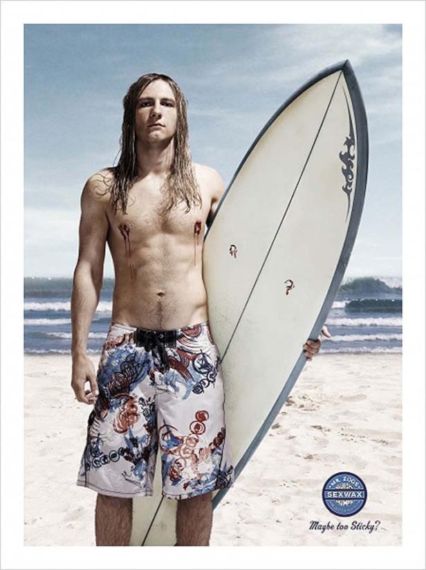 Ein blutverschmierter Surfer steht mit seinem Surfbrett am Strand.