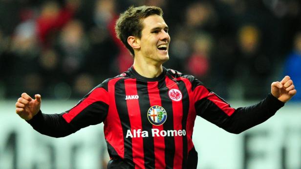 Ein lachender Fußballspieler im Trikot von Eintracht Frankfurt jubelt mit erhobenen Armen.