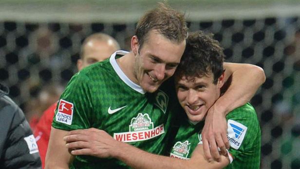 Zwei Fußballspieler von Werder Bremen umarmen sich auf dem Spielfeld.