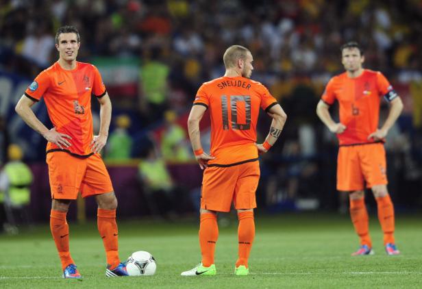 Drei niederländische Fußballspieler in orangefarbenen Trikots stehen auf dem Rasen.