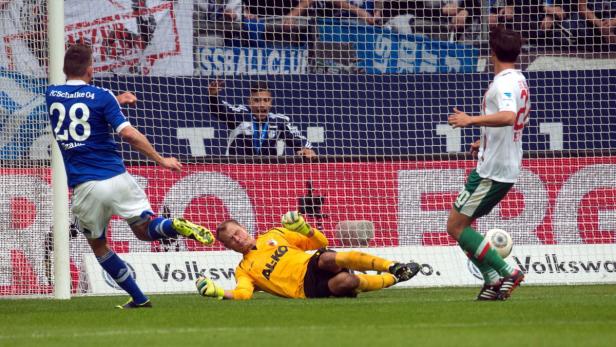 Ein Fußballspieler von Schalke 04 schießt auf das Tor, während der Torwart versucht, den Ball abzuwehren.