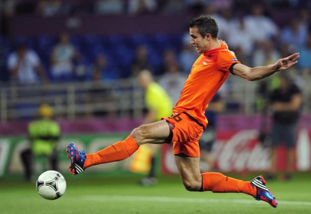 Ein Fußballspieler in orangefarbener Uniform schießt einen Ball.