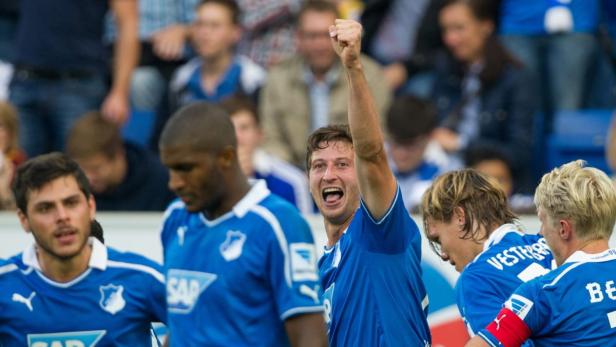 Ein jubelnder Fußballspieler im blauen Trikot mit erhobenem Arm.