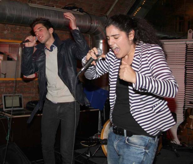 Ein Mann und eine Frau singen in einem Club in Mikrofone.