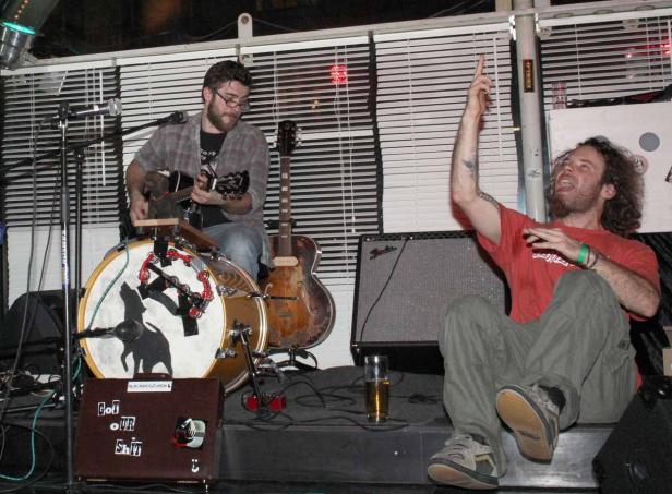 Zwei Männer treten mit Gitarre und Schlagzeug in einer Bar auf.