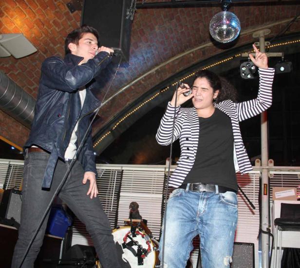 Zwei Sänger treten auf einer Bühne mit Mikrofonen und einer Discokugel auf.