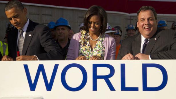 Barack Obama, Michelle Obama und Chris Christie bei einer Veranstaltung mit dem Wort „World“ im Vordergrund.
