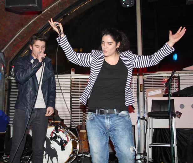 Eine Frau mit gestreiftem Blazer und ein Mann singen auf einer Bühne.