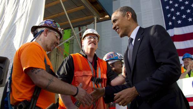 Barack Obama schüttelt Bauarbeitern die Hände vor einer amerikanischen Flagge.