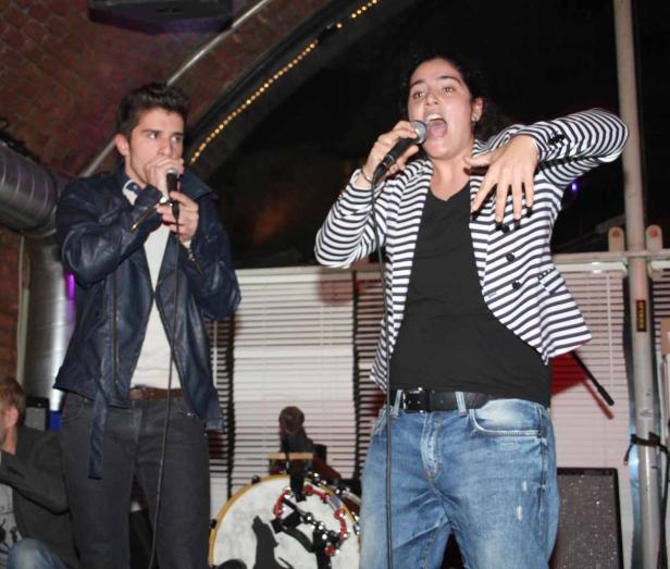 Zwei Personen treten mit Mikrofonen auf einer Bühne auf.