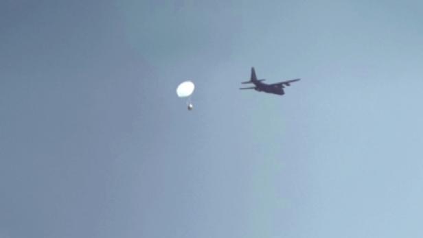 Ein Frachtflugzeug wirft eine Ladung mit einem Fallschirm ab.