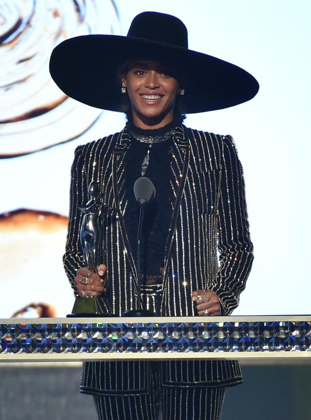 Beyoncé auf einer Bühne mit einem großen Hut und einem glitzernden Anzug, die eine Auszeichnung entgegennimmt.