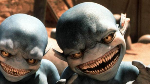 Zwei boshaft grinsende, blauhäutige Aliens mit spitzen Zähnen blicken in die Kamera.
