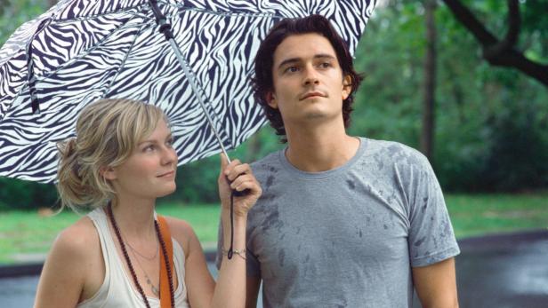 Kirsten Dunst und Orlando Bloom stehen unter einem Zebra-Regenschirm.