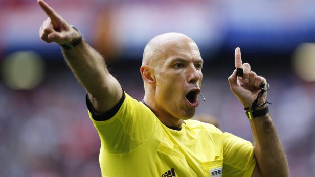 Ein Schiedsrichter in gelbem Trikot zeigt mit beiden Händen nach oben.