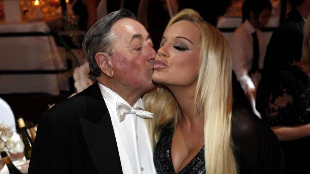 Ein älterer Mann und eine blonde Frau geben sich einen Kuss.