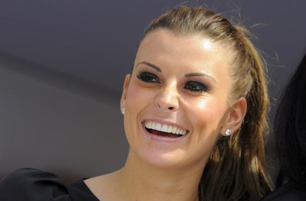 Eine lächelnde Frau mit dunklem Augen-Make-up und Ohrringen.