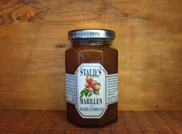 Ein Glas Marillenmarmelade mit Marillenbrand von Staud’s vor einem Holzbrett.