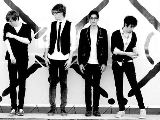 Vier junge Männer posieren vor einer Wand mit abstrakten Mustern.