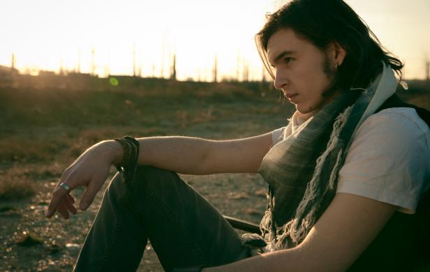 Ein junger Mann mit langem Haar sitzt nachdenklich in der Abendsonne.