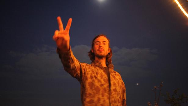 Ein Mann zeigt bei Nacht das Victory-Zeichen in den Himmel.